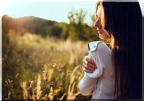 Woman in profile out in sunny nature area holding her shoulder