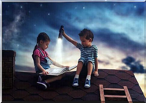 A boy holds a flashlight so a girl can read a book on a roof