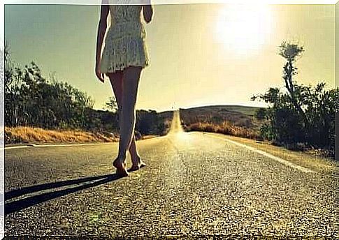 A woman follows a long, lonely road barefoot towards the sunshine of dawn